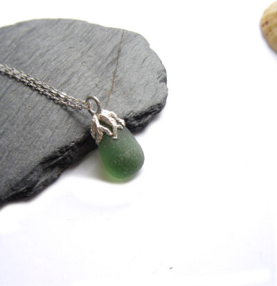 Coastal Inspired Green Seaglass Necklace on a piece of sea shale with a limpet shell in the background. A nature-inspired necklace in authentic seaglass collected by hand on the Northumbrian coast of England. The sea glass is set in silver which I have handcrafted in an original design to resemble seaweed fronds. Men's and women's jewellery by Northumbria Gems.