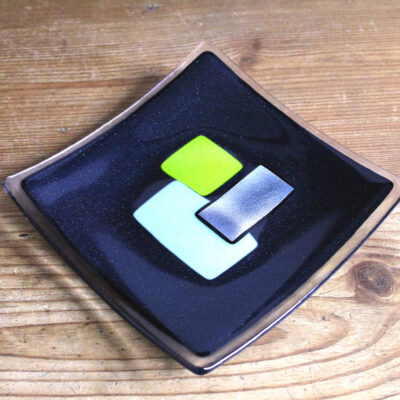 Geometric glass dish in lime, mint and silver on blue, handcrafted using fused glass techniques. Retro dish with green sections intersected with silver.