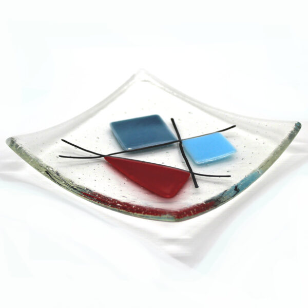 Geometric glass dish red and blues on clear. A sixties retro dish with coloured shapes intersected with black lines. Handcrafted using fused glass techniques. Made in England.