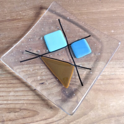 Geometric 60s retro glass dish in tan and blues on clear handcrafted using fused glass techniques. Blue and tan shapes are intersected with black lines.