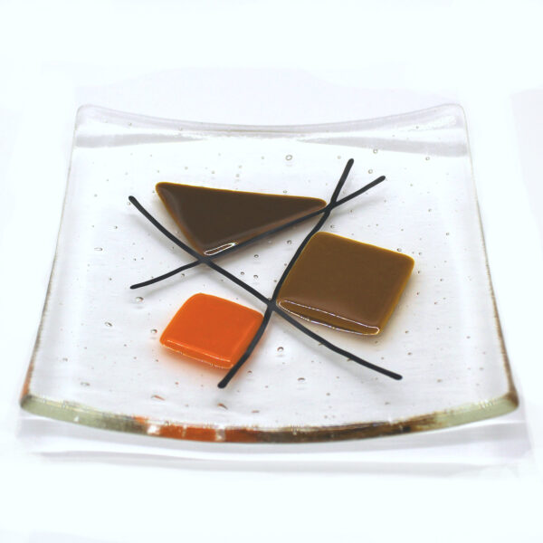 Geometric glass dish tan and orange on clear. A sixties retro dish with tan, brown and orange shapes intersected with black lines. Handcrafted using fused glass techniques. Made in England.