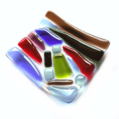 Multicoloured fused glass dish of irregular coloured shapes in red, green, blues and brown on a clear background. Ornamental glassware handcrafted in the north of England by Northumbria Gems.