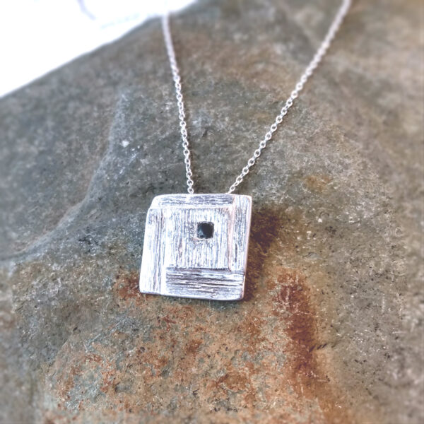 Whitby Jet Inlaid Silver Geometric Pendant. The pendant is square in shape with a stepped, spiral effect design and handcrafted in ethical silver, with a hidden bail at the back. The tiny square cabochon has been handcrafted in genuine Whitby jet. Made in the north-east of England.