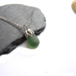 Coastal Inspired Green Seaglass Necklace on a piece of sea shale with a limpet shell in the background. A nature-inspired necklace in authentic seaglass collected by hand on the Northumbrian coast of England. The sea glass is set in silver which I have handcrafted in an original design to resemble seaweed fronds. Men's and women's jewellery by Northumbria Gems.