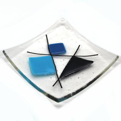 Geometric glass dish in aventurine and blues on a clear background. A sixties retro dish with coloured shapes intersected with black lines. Handcrafted using fused glass techniques. Made in England.