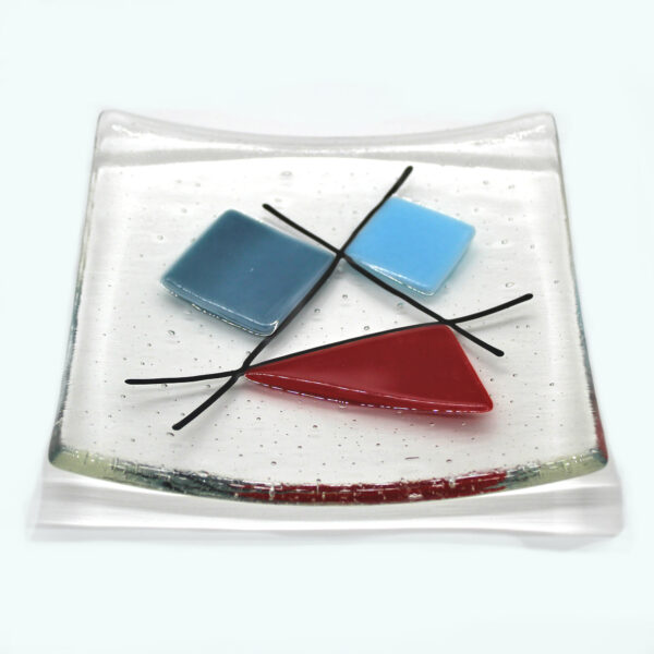 Geometric glass dish red and blues on clear. A sixties retro dish with coloured shapes intersected with black lines. Handcrafted using fused glass techniques. Made in England.