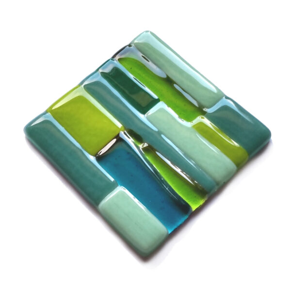 Shades of green fused glass coaster. A small ornamental glass coaster handcrafted using fused glass techniques. The design is abstract irregular green shapes on a clear background. To rest a cup or mug on or to add interest and coloured accents to your room. Handmade in England by Northumbria Gems.