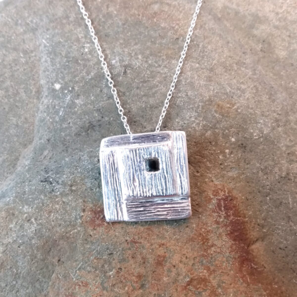 Whitby Jet Inlaid Silver Geometric Pendant. The pendant is square in shape with a stepped, spiral effect design and handcrafted in ethical silver, with a hidden bail at the back. The tiny square cabochon has been handcrafted in genuine Whitby jet. Made in the north-east of England.