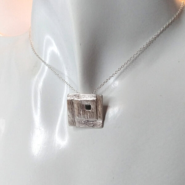 Whitby Jet Inlaid Silver Geometric Pendant. The pendant is square in shape with a stepped, spiral effect design and handcrafted in ethical silver, with a hidden bail at the back. The tiny square cabochon has been handcrafted in genuine Whitby jet. Made in the north-east of England.